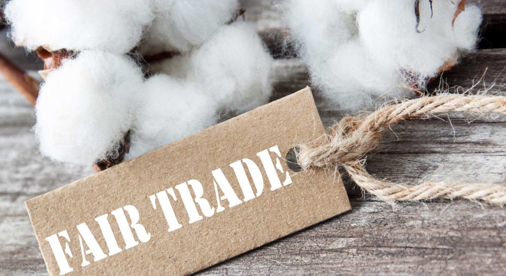 fair trade written on a cardboard piece surrounded with cotton and placed on a table of light wooden color